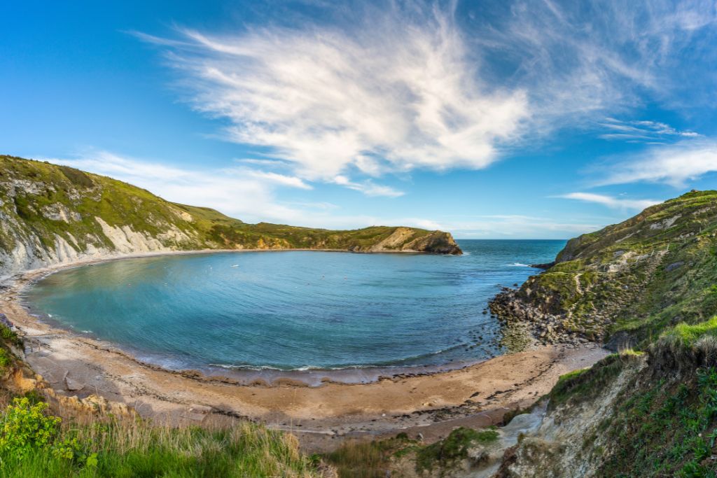 Blue water in a cove surrounded by cliffs of rock and green grass.