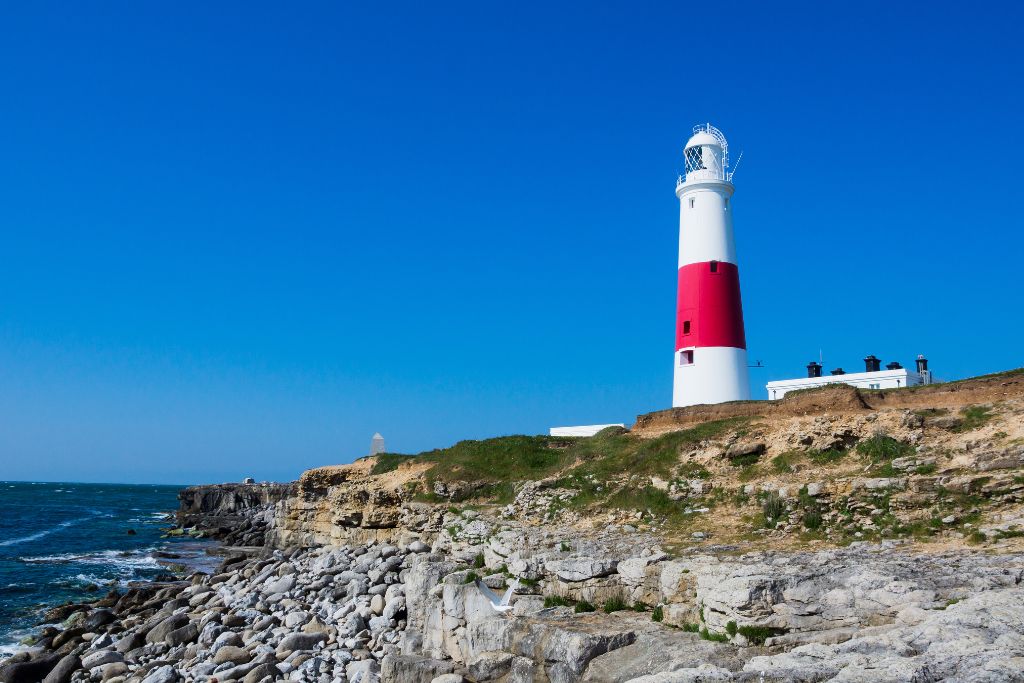 Red and white lighthouse on a rocky cliff facing the ocean.